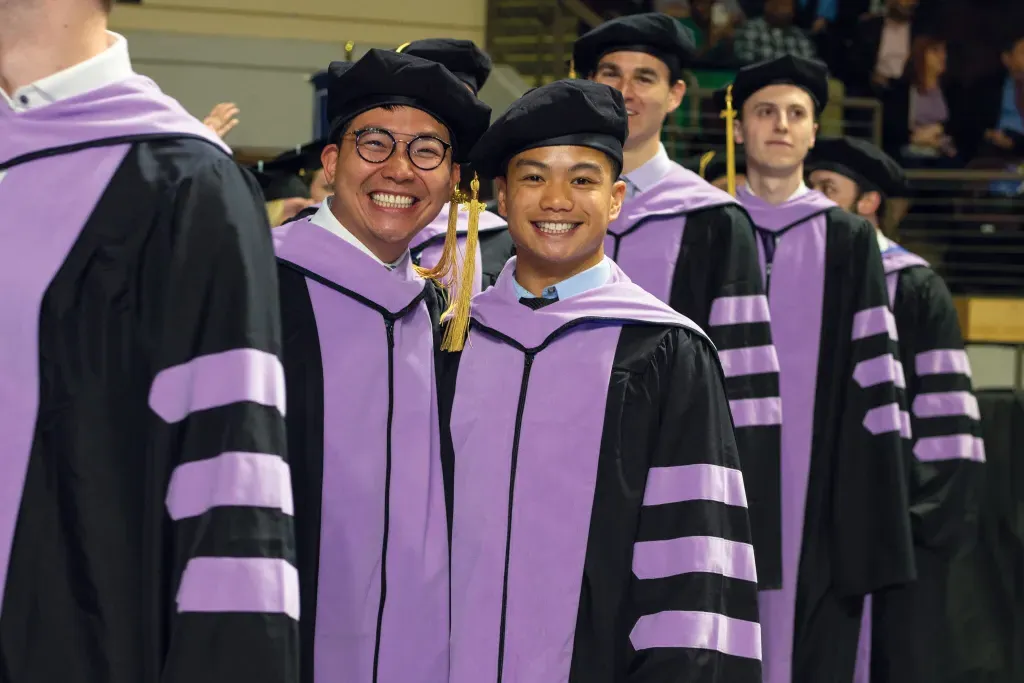 Two students stand in like to walk across the stage at the 2023 U N E commencement ceremony