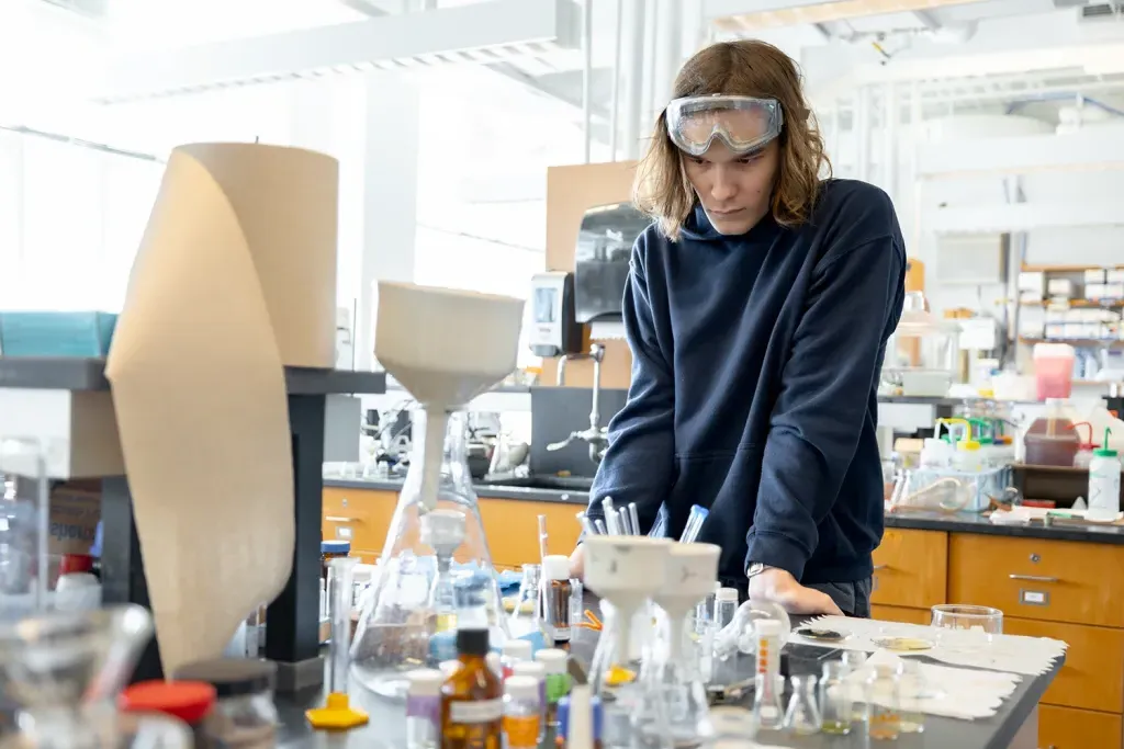 A U N E student stands and stares at a beakers and samples in a lab