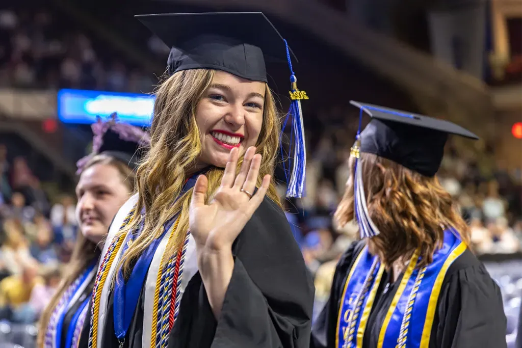 A U N E graduate smiles and waves at the camera