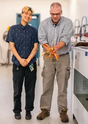 Markus Frederich holding a lobster standing next to Ruby Motulsky in the lab