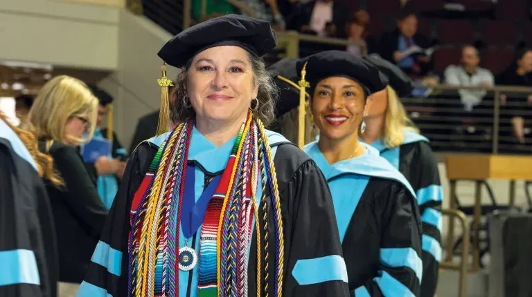 A graduating student smiles for the camera while waiting to cross the stage at commencement